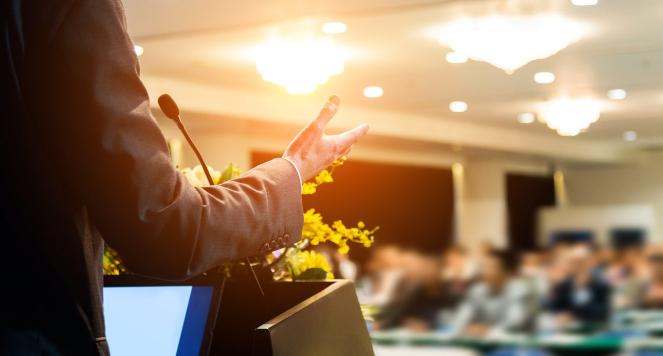 Business man making a speech in front of audience at conference hall.