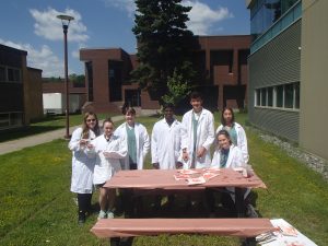 Campers pose for photo at picnic table outside in CSI lab coats