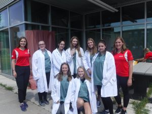 Campers in CSI lab coats pose for photo with team leads ouside of medical school building