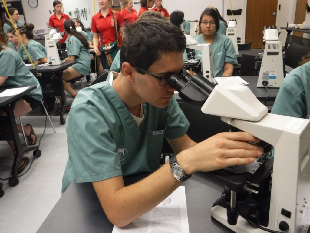 Close up of a camper using a microscope in the lab with other campers and team leads in the background