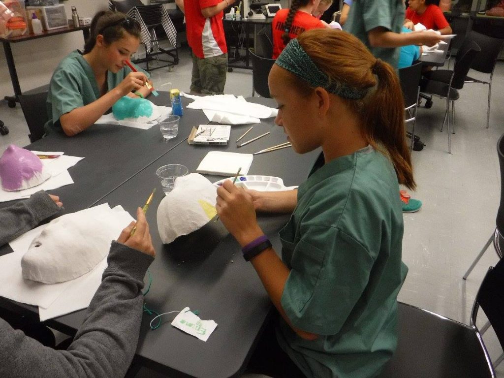 Campers sitting at a table in the lab decorating masks with paint