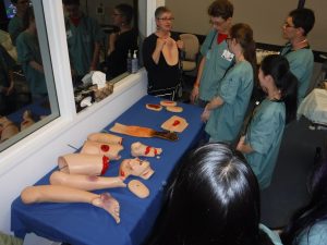 NOSM Staff member instructing campers on wounds using SimMan 3G body parts.
