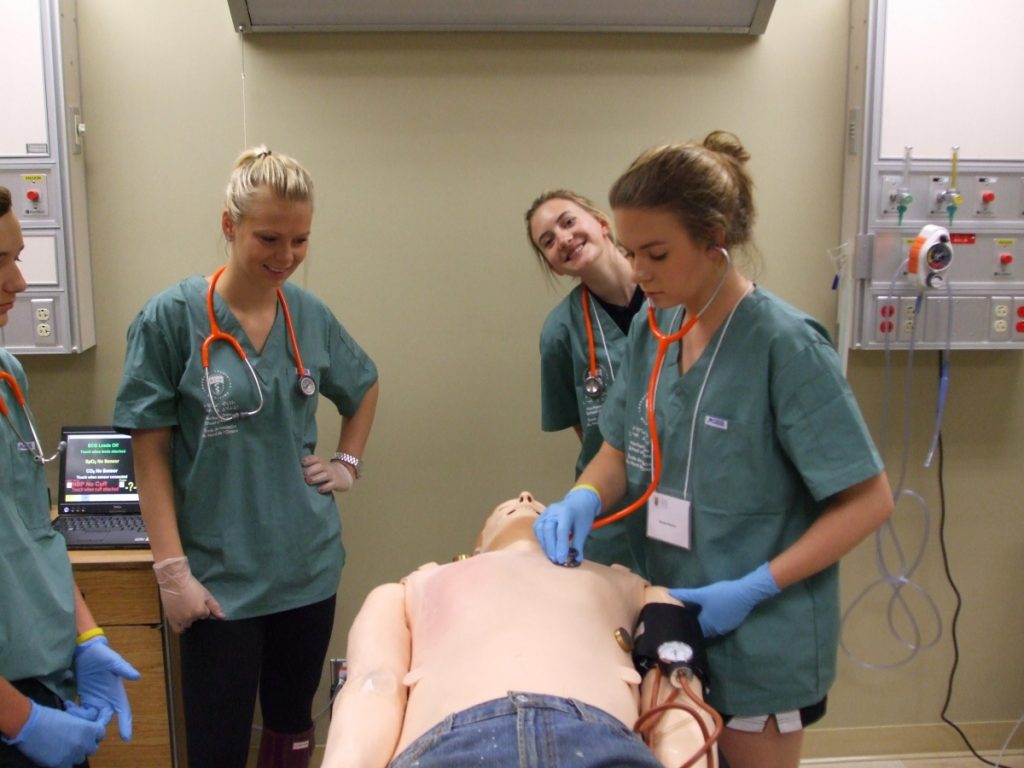 Camper using stethescope on SimMan 3G simulation mannequin while fellow campers look on