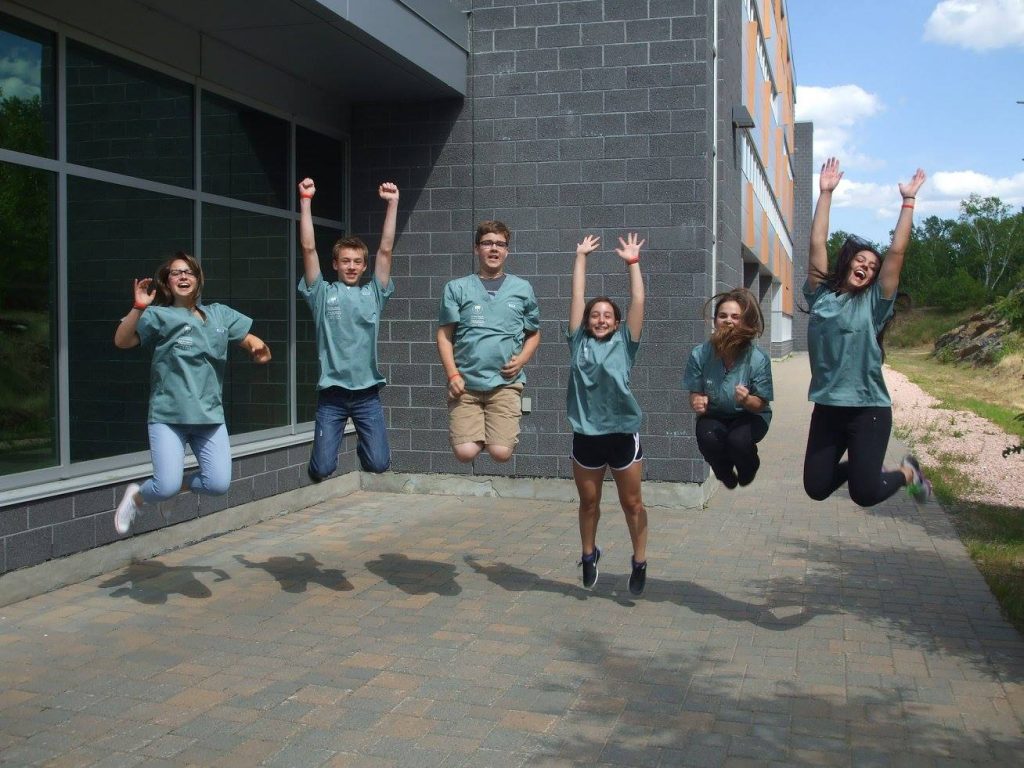 Campers pose for photo by jumping into the air outside of medical school building