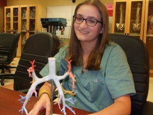Camper poses for picture with model of heart arteries and veins in lab