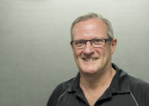 Professional headshot of Dr. Gregory Ross in front of a beige background