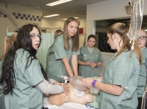 Camper performing CPR on SimMan 3G simulation mannequin while two fellow campers ventilate and other camper looks on in background