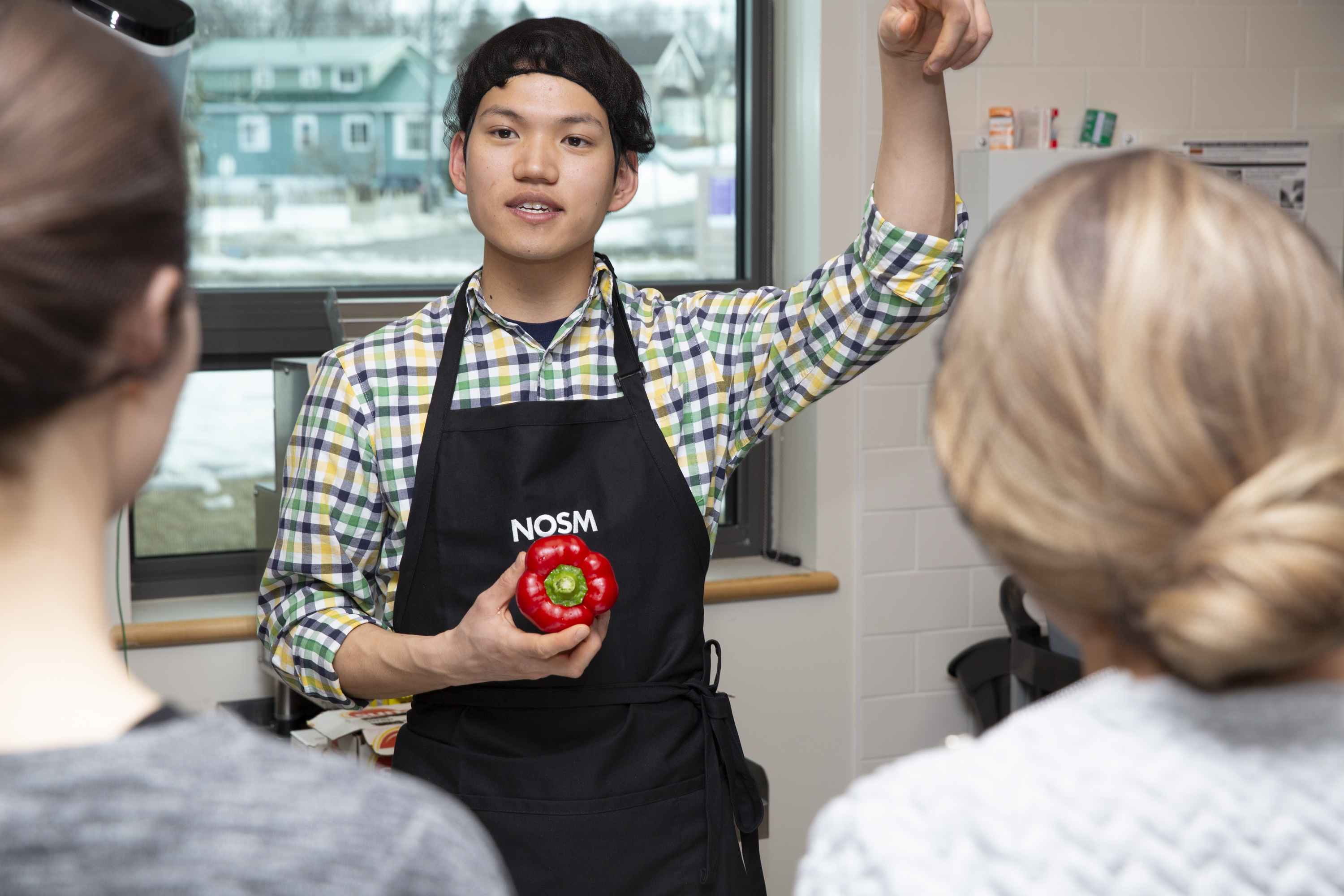 Photo of man wearing a NOSM apron and holding a red pepper in a kitchen.