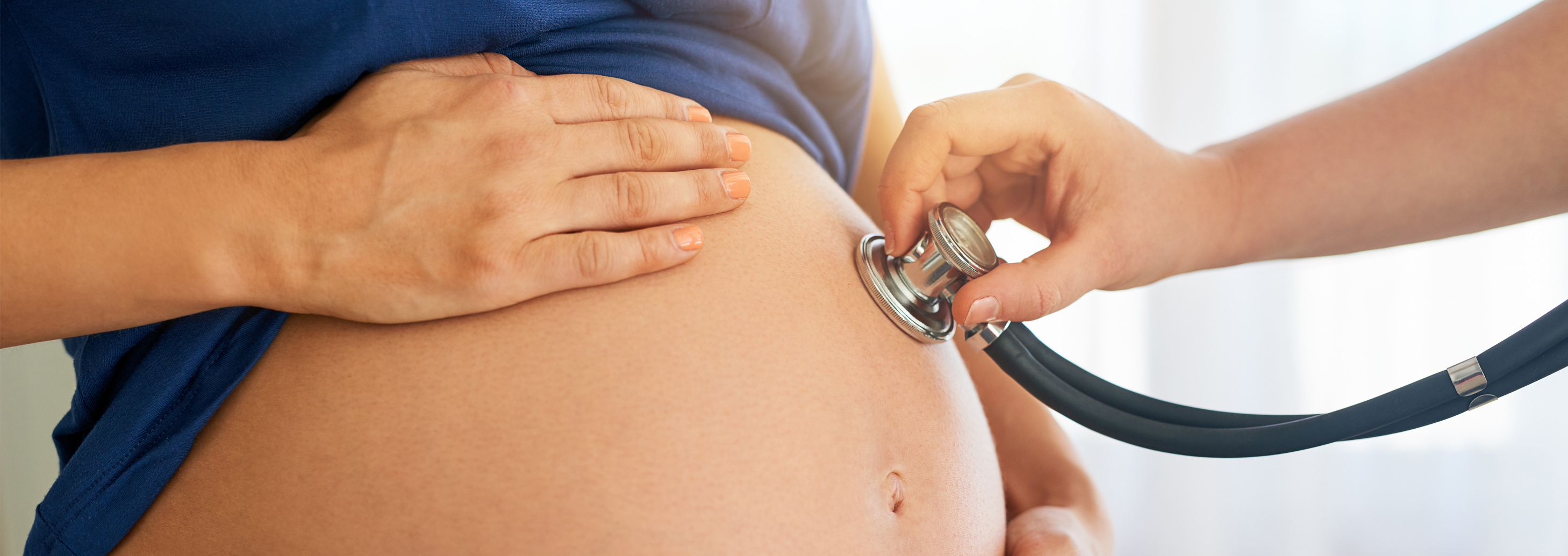 Photo of hand holding a stethoscope to a pregnant woman's bare stomach.