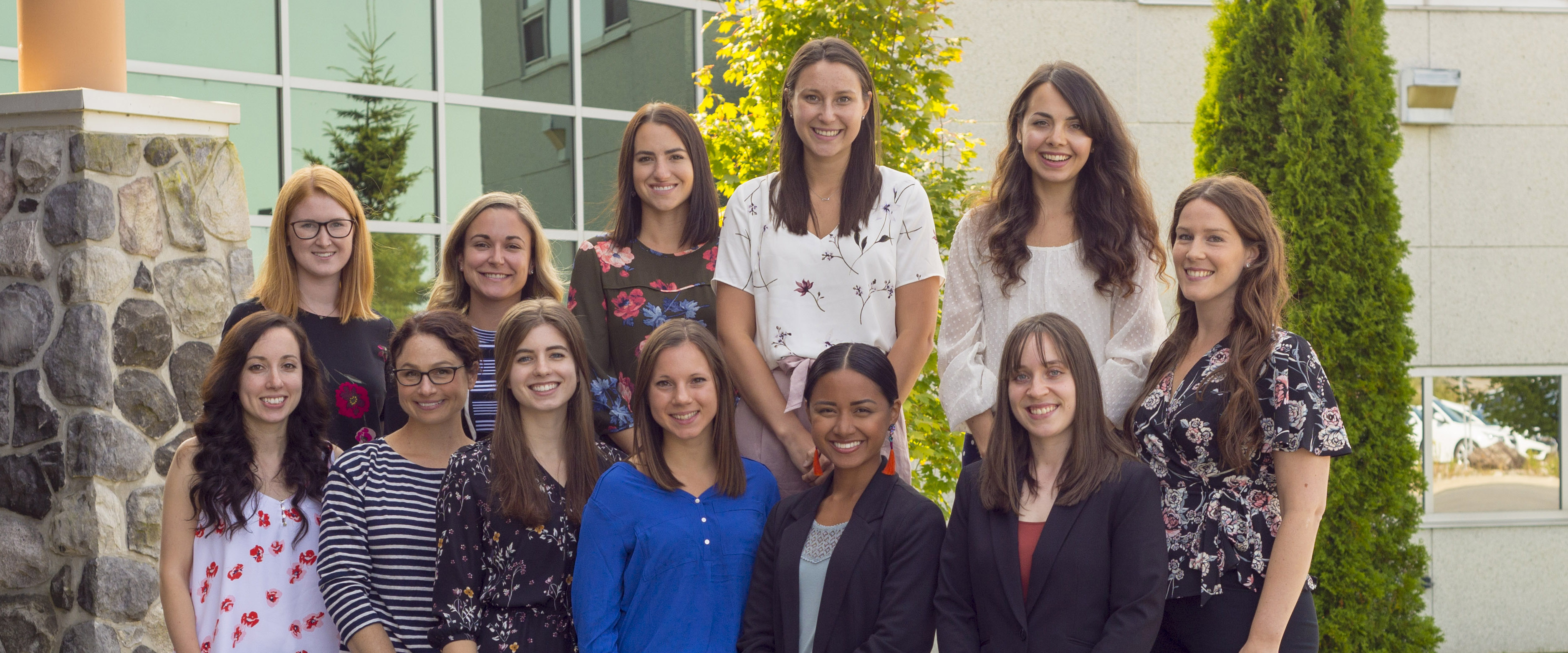 Photo of 12 dietetic interns sitting or standing on the rocks near the front of the medical school building in Sudbury.