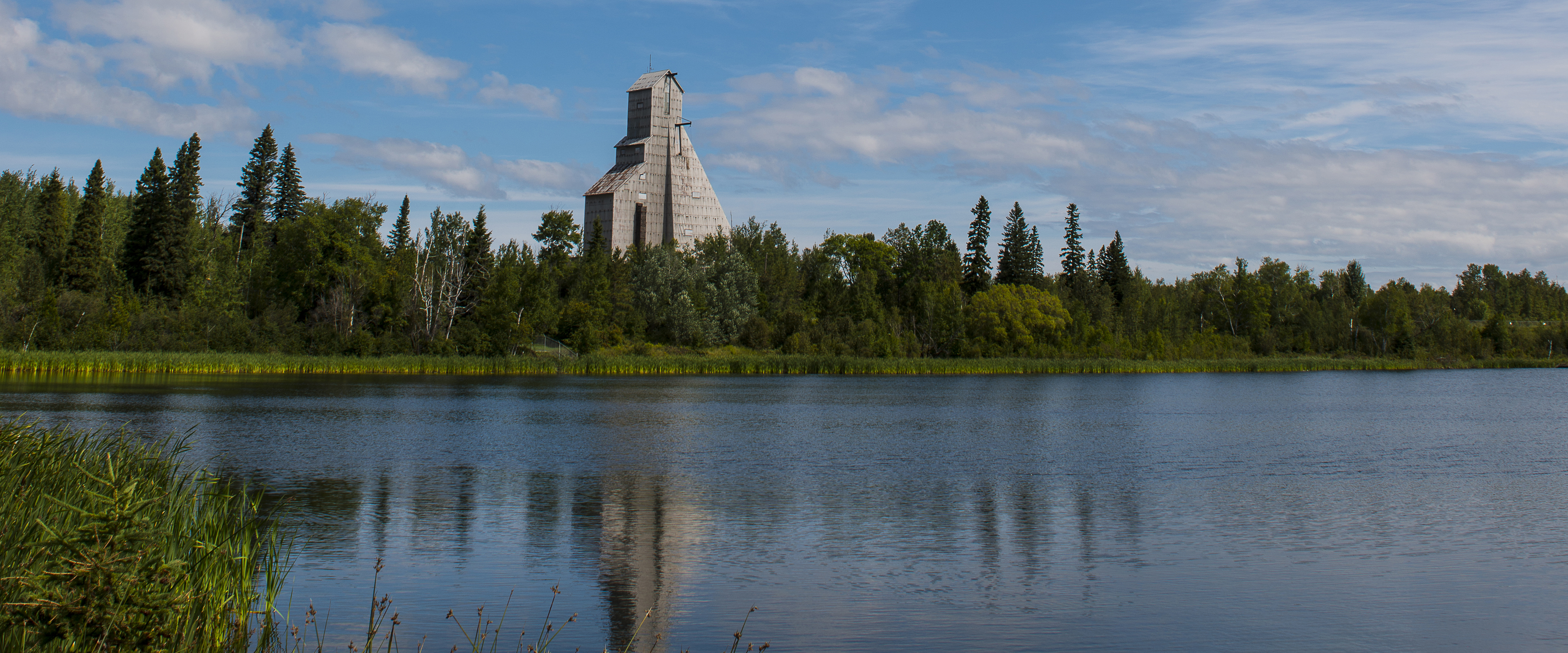 Photo of a lake in Timmins, Ontario, with a mine headframe in the background.