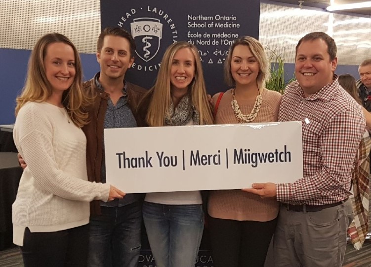 Graduates holding a sign that reads Thank you, Merci, Miigwetch