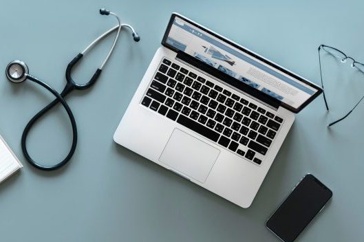 laptop on desk with stethoscope and a pair of glasses beside the computer