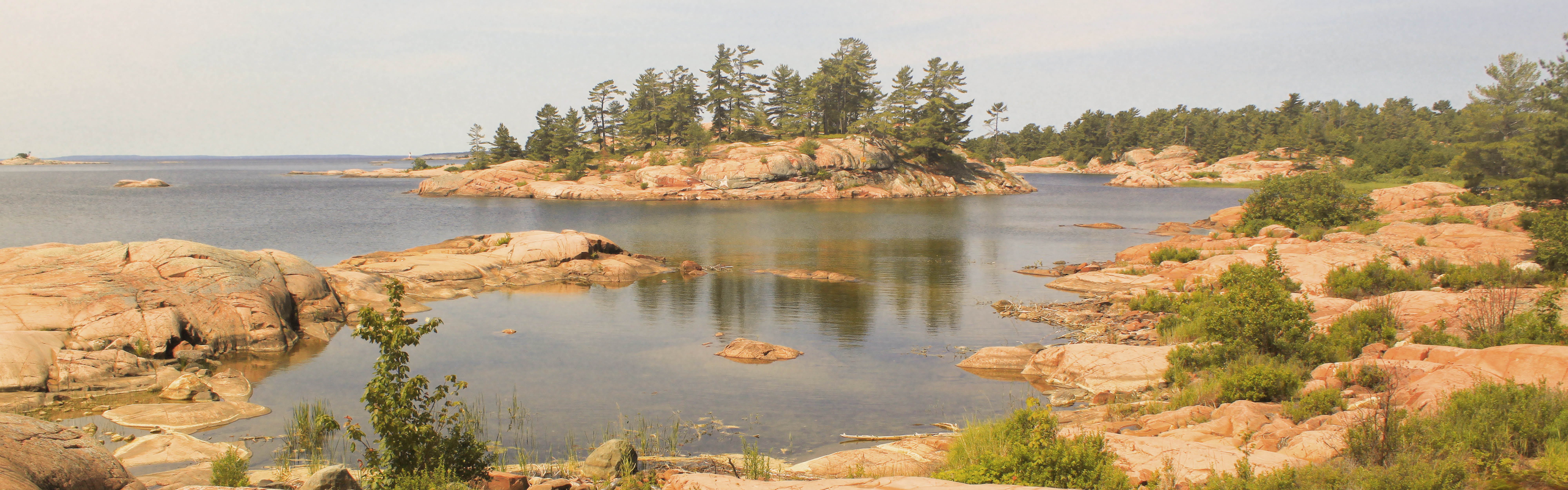 Photo of Northern Ontario Lake, with a rocky shoreline and large pine trees off in the distance.