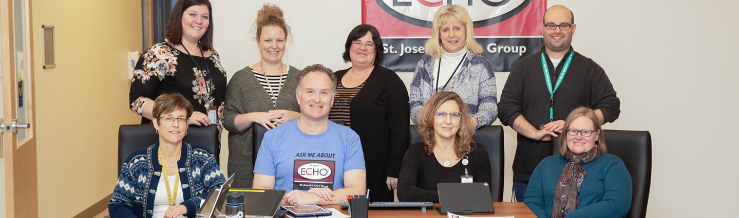 Group of nine men and women sitting and standing in front of red banner with ECHO logo