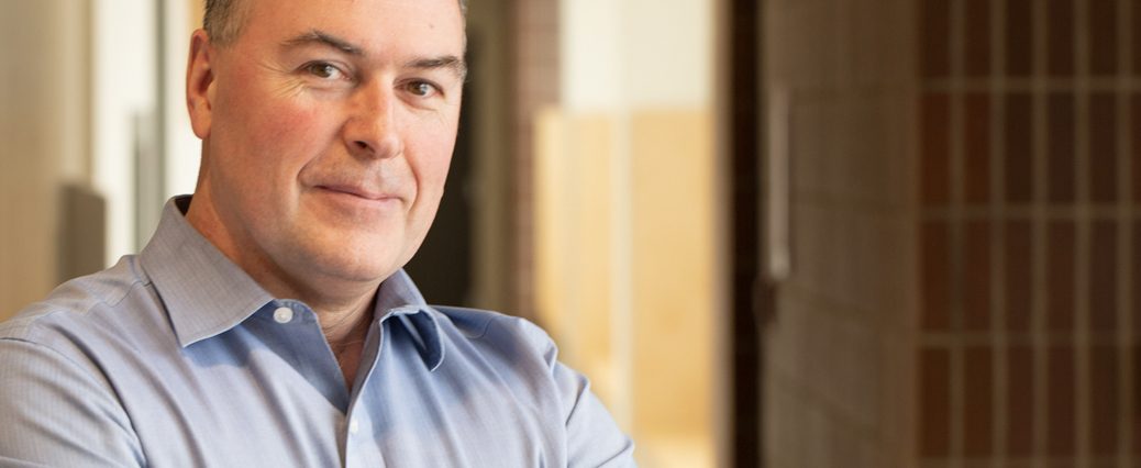 Man in blue shirt, smiling, stands in hospital hallway