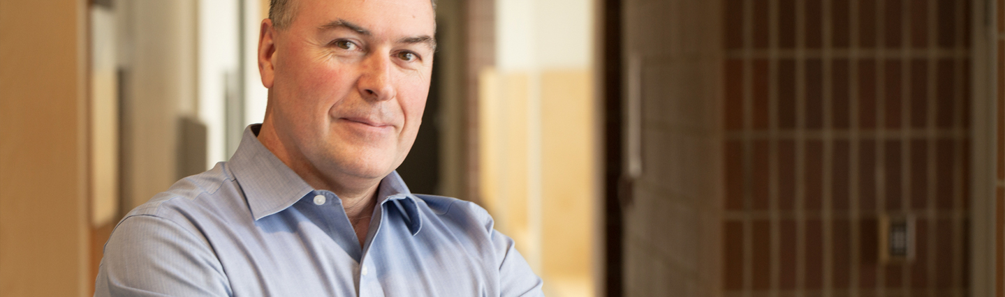 Man in blue shirt, smiling, stands in hospital hallway