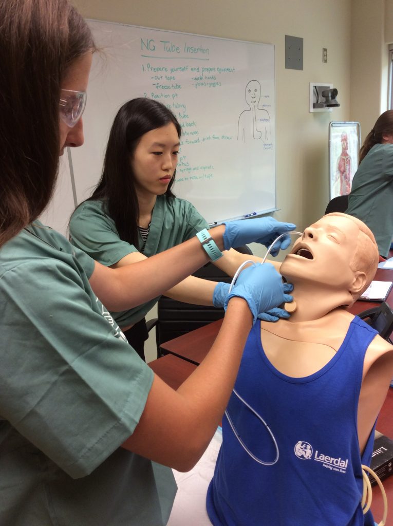 Two campers practice inserting a naso-gastric tube into simulation mannequin.