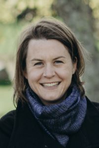 Dr. Emily Groot is smiling and wearing a black coat with a blue scarf.