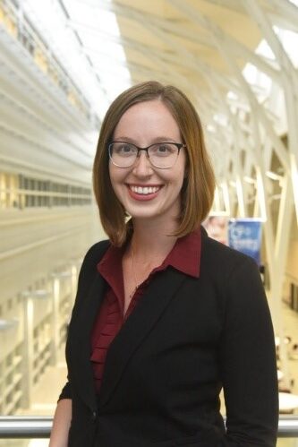 Dr. Emma Pillsworth is smiling wearing glasses, a black blazer jacket and a red collard shirt 