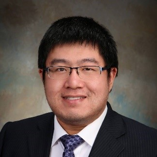 Dr. Stone Li is smiling, wearing glasses, a black blazer jacket and with collard shirt with checkered tie