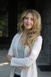 Dr. Melanie Squarzolo is smiling with arms crossed, wearing a white blazer jacket and light blue shirt 