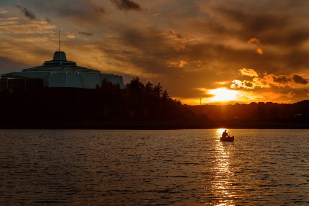 Sunset picture of Ramsey Lake in Sudbury Ontario, facing the Science North building, and a canoer is on the lake.