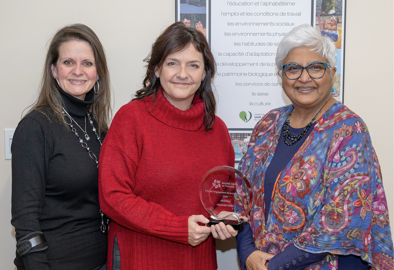 Three women smile as they pose with an award. The award, a circular glass trophy, is held by the woman in the centre.