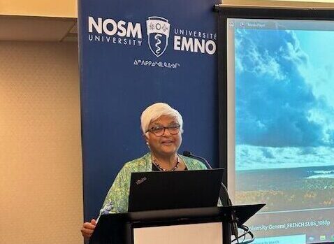 Dr. Sarita Verma standing behind a podium speaking.