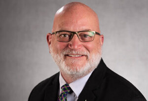 Dr. David Marsh looks at the camera with a small smile. He wears a black suit jacket and glasses. He has a short white beard and moustache. 