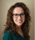 Caucasian woman with brown curly hair and glasses.