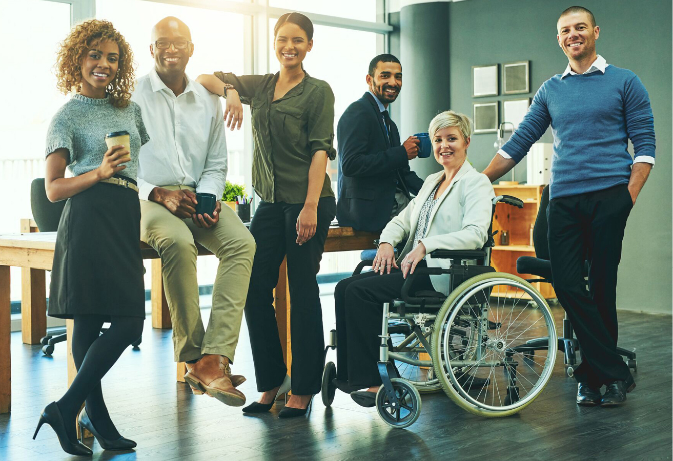 group of people in a room standing or sitting around a large table with one person in a wheel chair