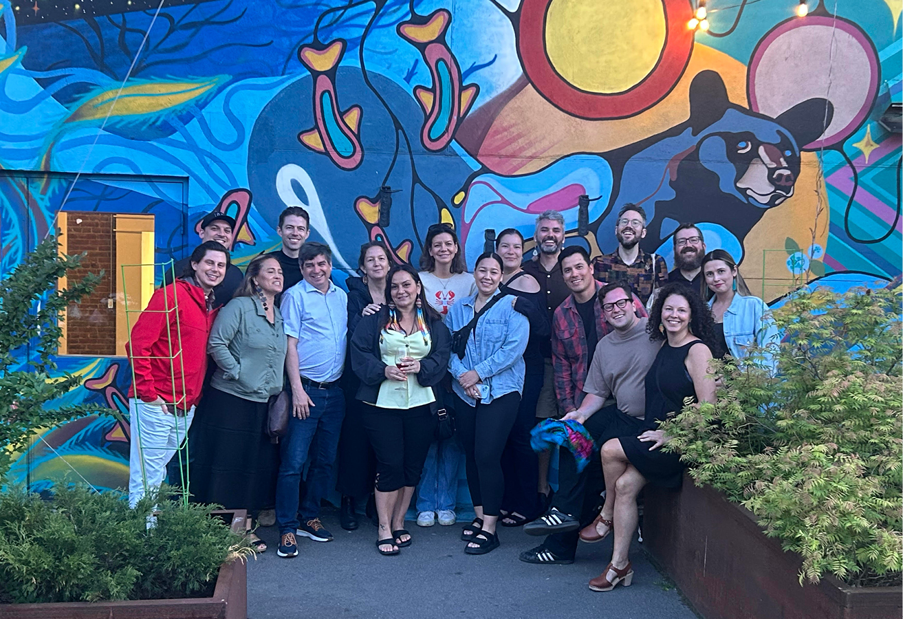 A group of people pose in front of a mural in the Woodlands style.
