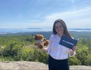 Claire Poulin tient une carte indiquant « #YesToNOSMU » et Dr DesBois, un orignal en peluche portant un t-shirt de l'Université de l'EMNO. Le Sleeping Giant est en arrière-plan.