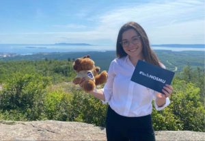 Claire Poulin tient une carte indiquant « #YesToNOSMU » et Dr DesBois, un orignal en peluche portant un t-shirt de l'Université de l'EMNO. Le Sleeping Giant est en arrière-plan.