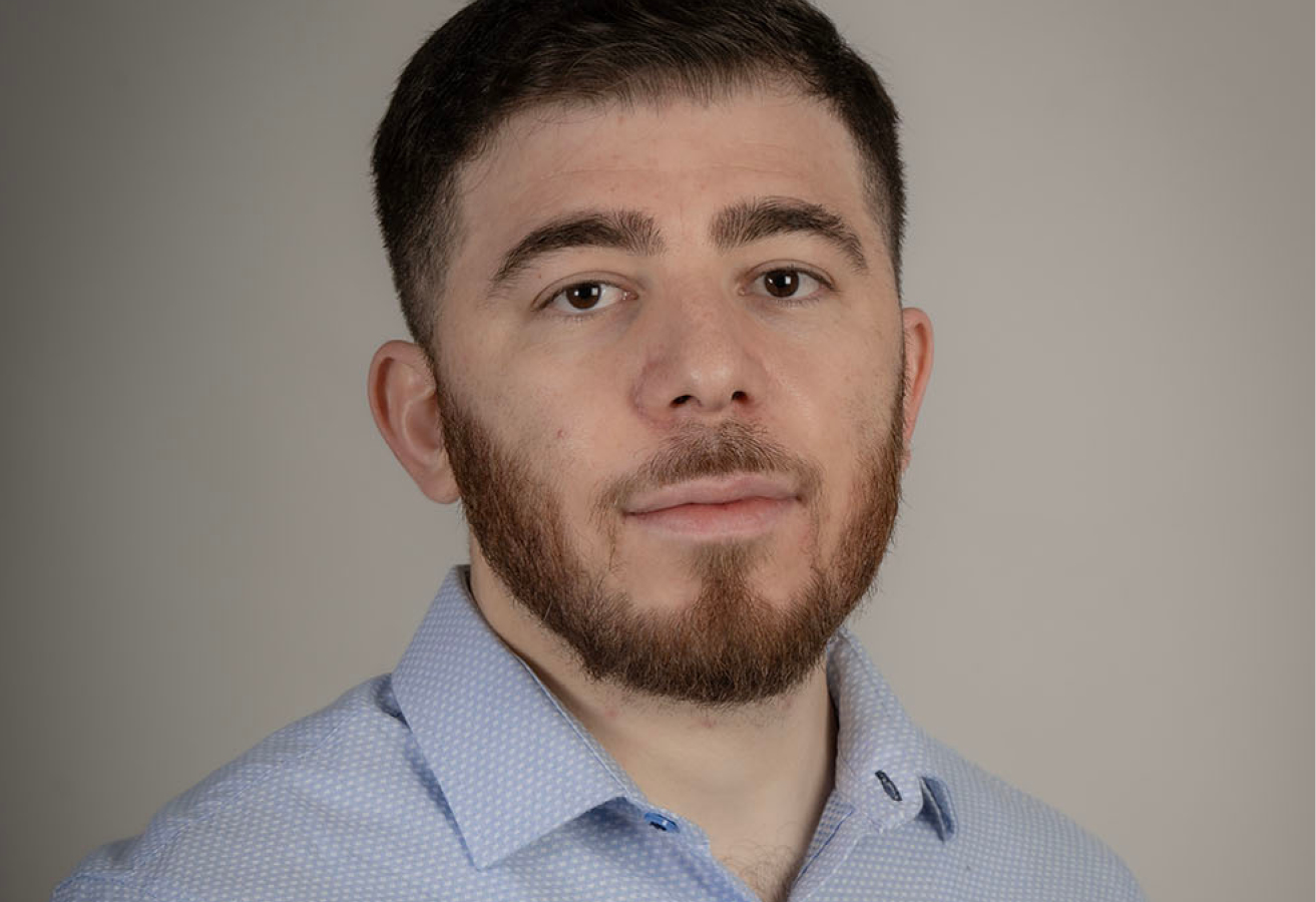 Mohamed Alzahran wears a light blue button-down shirt. He has a close-cropped beard and short brown hair. Mohamed Alzahran porte une chemise bleu clair et a une barbe rasée de près et les cheveux bruns courts.